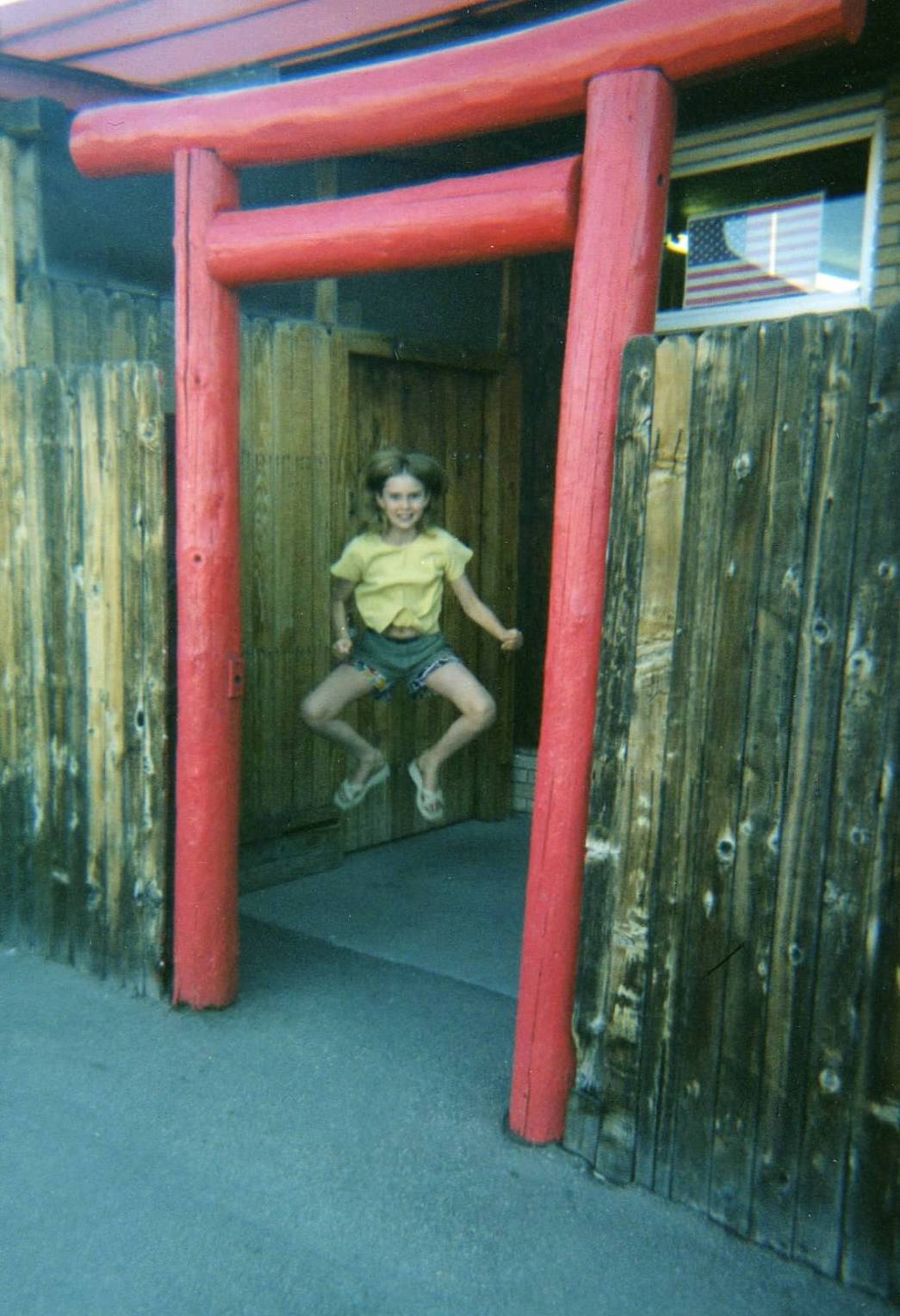 child Holly - leaping off the ground framed by the torii of the dojo - American flag in the window